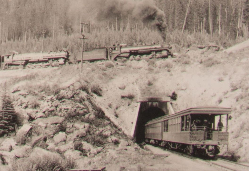 Photo of old locomotive passing over one of the tunnels as passenger cars enter the tunnel